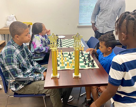 Group of kids watching two kids play chess