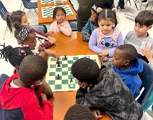 Group of young children sitting around a table playing chess